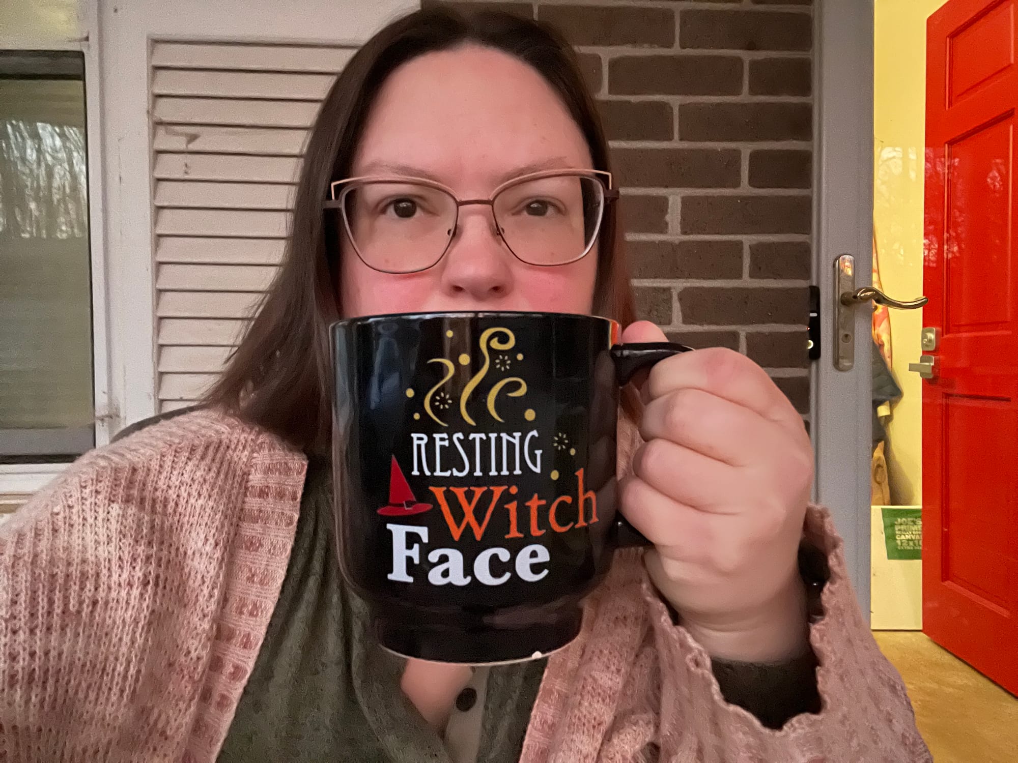 A middle-aged white woman with shoulder-length brown hair, glasses, and a too-big coffee cup with the text "Resting Witch Face."